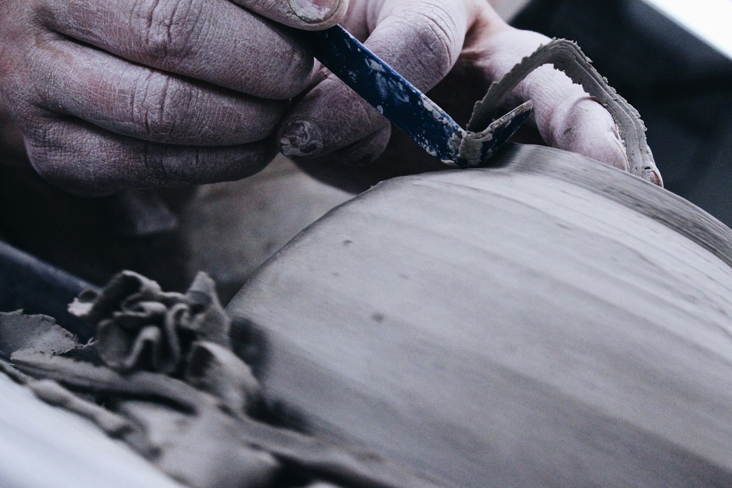 Hands shaping wet clay with a blue pottery tool.